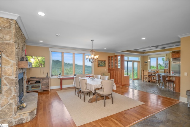 dining room featuring crown molding, recessed lighting, a stone fireplace, and a notable chandelier