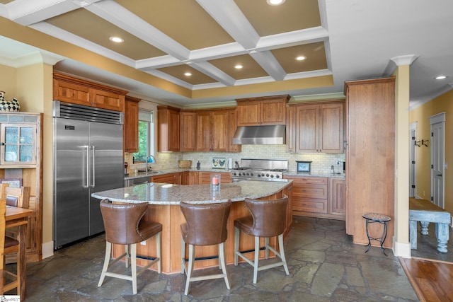 kitchen with range, a sink, stone tile flooring, under cabinet range hood, and stainless steel built in refrigerator