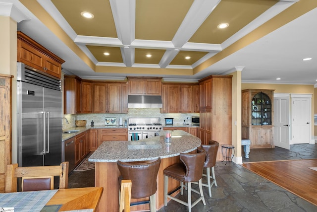 kitchen with a center island, a sink, premium appliances, under cabinet range hood, and stone tile floors