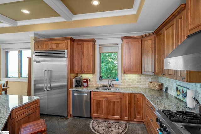 kitchen featuring brown cabinetry, ventilation hood, a sink, backsplash, and stainless steel appliances