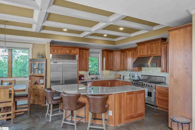 kitchen with stone tile flooring, coffered ceiling, under cabinet range hood, and high quality appliances