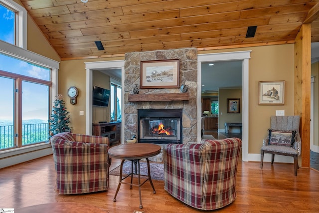 living area with a stone fireplace, baseboards, wooden ceiling, wood finished floors, and vaulted ceiling
