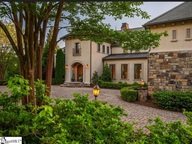 back of property featuring stone siding, stucco siding, a chimney, a standing seam roof, and metal roof