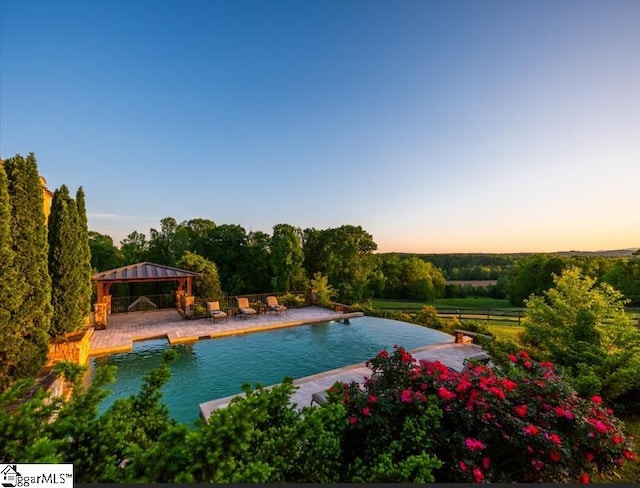 pool at dusk with a gazebo, an outdoor pool, fence, and a patio