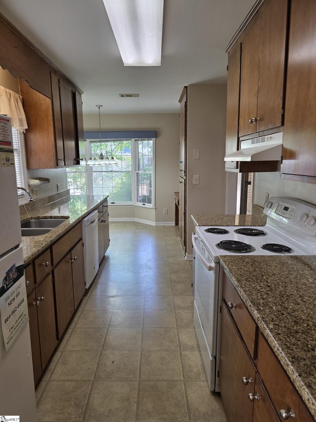 kitchen featuring visible vents, a sink, baseboards, under cabinet range hood, and white appliances