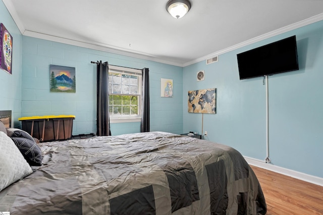 bedroom featuring baseboards, ornamental molding, wood finished floors, and visible vents
