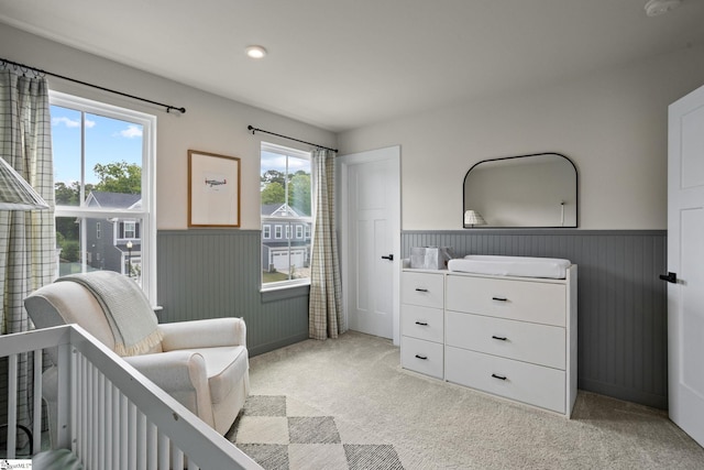 bedroom with light colored carpet, recessed lighting, a wainscoted wall, and a nursery area