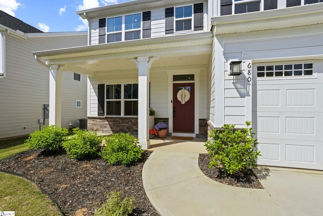 entrance to property featuring a porch, stone siding, central air condition unit, and a garage