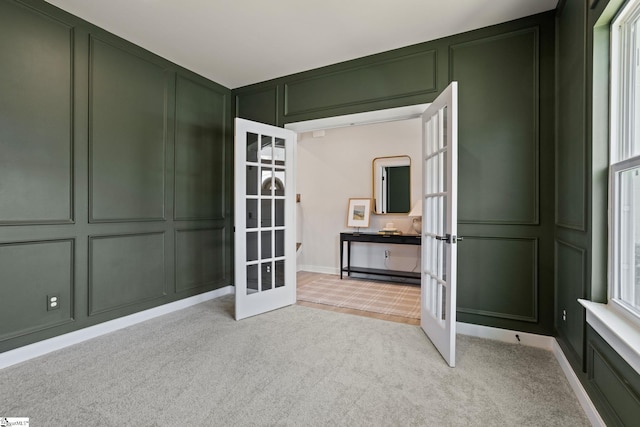 empty room featuring a decorative wall, light carpet, and french doors