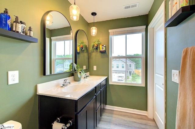 bathroom with double vanity, visible vents, wood finished floors, a sink, and baseboards