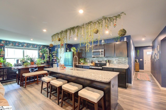 kitchen with a kitchen island with sink, a breakfast bar area, a sink, light wood finished floors, and appliances with stainless steel finishes