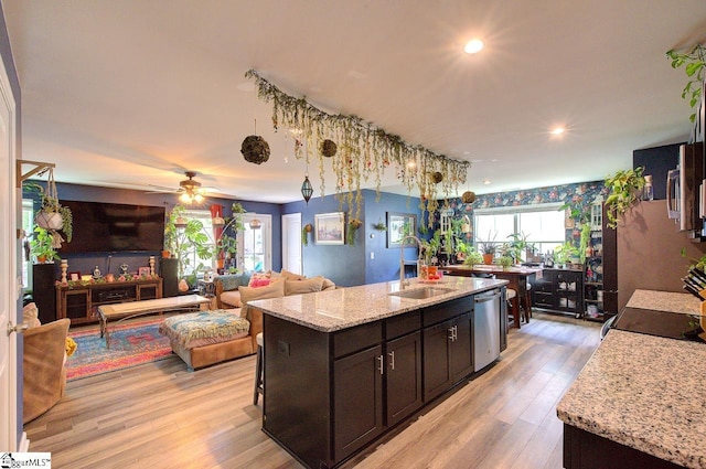 kitchen featuring a sink, light wood-style floors, dishwasher, open floor plan, and a center island with sink