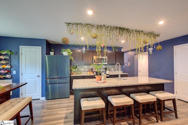 kitchen with appliances with stainless steel finishes, a breakfast bar, a sink, and light wood-style floors