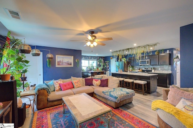 living room with visible vents, a ceiling fan, and light wood-type flooring
