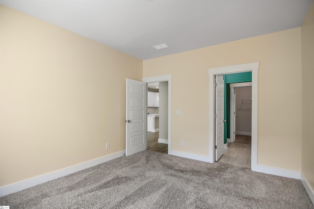 unfurnished bedroom with baseboards, visible vents, light carpet, and a walk in closet