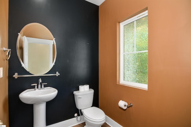 half bath featuring baseboards and toilet