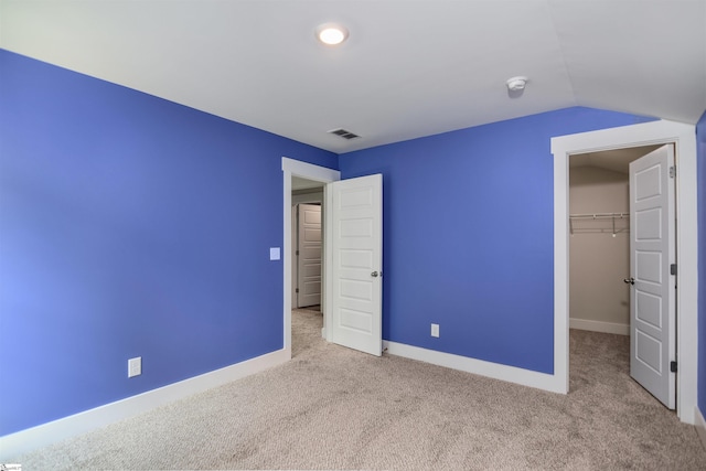 unfurnished bedroom with visible vents, a closet, carpet floors, a walk in closet, and vaulted ceiling