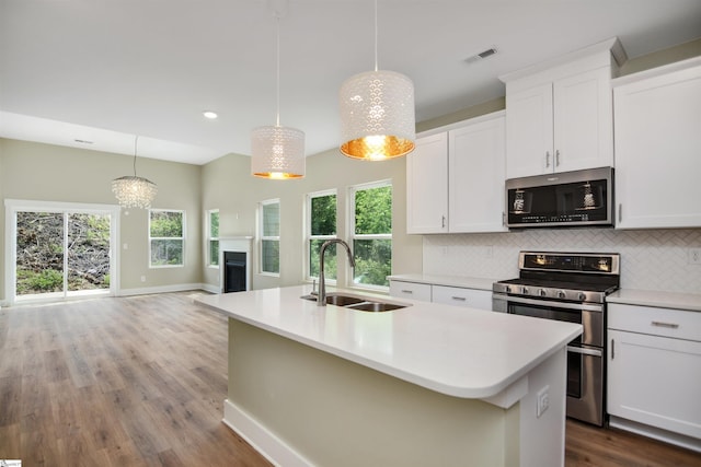 kitchen featuring appliances with stainless steel finishes, a sink, baseboards, tasteful backsplash, and a center island with sink