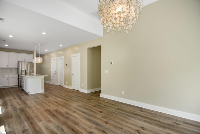 unfurnished living room with recessed lighting, baseboards, an inviting chandelier, and wood finished floors