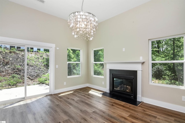 unfurnished living room featuring baseboards, a glass covered fireplace, wood finished floors, and a towering ceiling