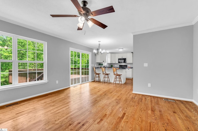 unfurnished living room with crown molding, ceiling fan with notable chandelier, baseboards, light wood-type flooring, and visible vents
