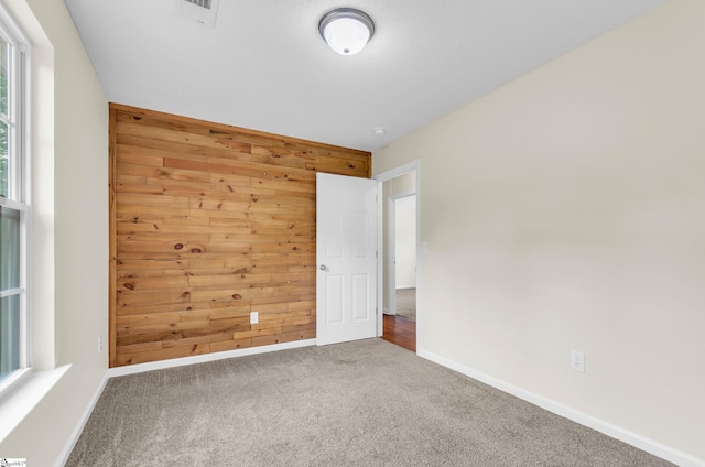 carpeted spare room with baseboards, wood walls, and visible vents