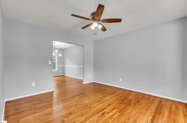 spare room with baseboards, ceiling fan with notable chandelier, and light wood-style flooring