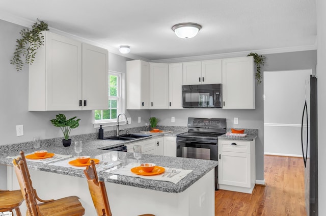 kitchen with a peninsula, white cabinetry, a sink, and black appliances