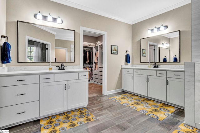 bathroom with wood tiled floor, crown molding, two vanities, a sink, and baseboards