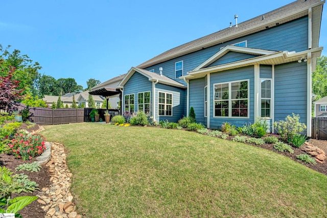rear view of house featuring a lawn and fence