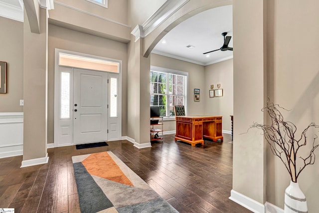 entrance foyer featuring crown molding, arched walkways, ceiling fan, and dark wood finished floors