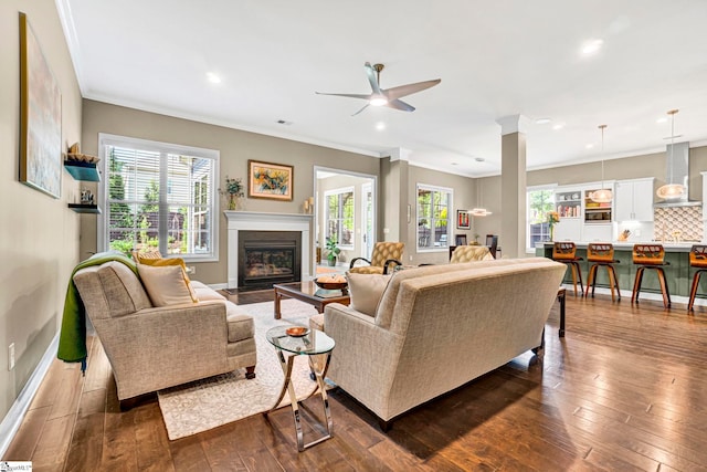 living room with plenty of natural light, a ceiling fan, a glass covered fireplace, and dark wood-style floors