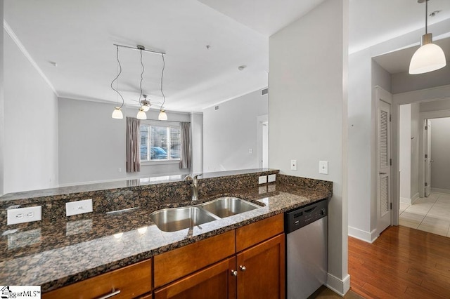kitchen with brown cabinets, a sink, light wood finished floors, dark stone countertops, and stainless steel dishwasher