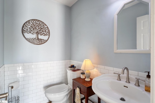 bathroom featuring toilet, tile walls, a sink, and a wainscoted wall