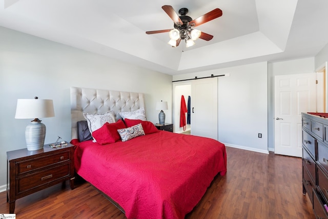 bedroom with dark wood-style flooring, baseboards, a barn door, and a raised ceiling