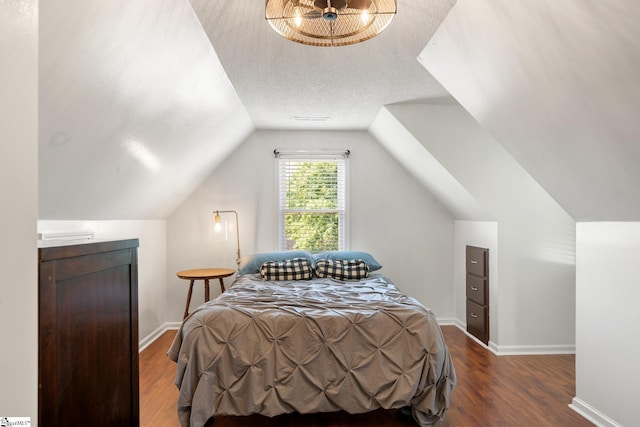 bedroom with visible vents, wood finished floors, baseboards, a textured ceiling, and vaulted ceiling