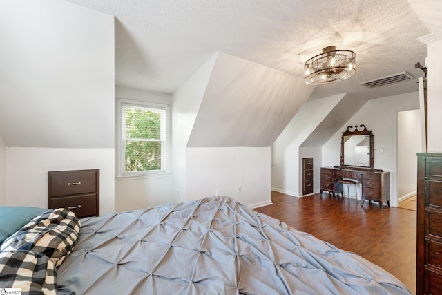 bedroom featuring visible vents, a textured ceiling, wood finished floors, and vaulted ceiling
