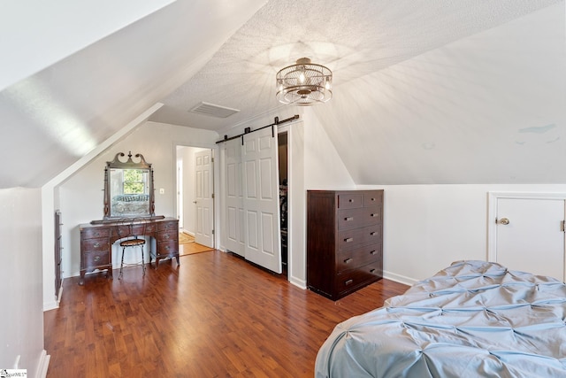 bedroom featuring vaulted ceiling, a barn door, wood finished floors, and visible vents