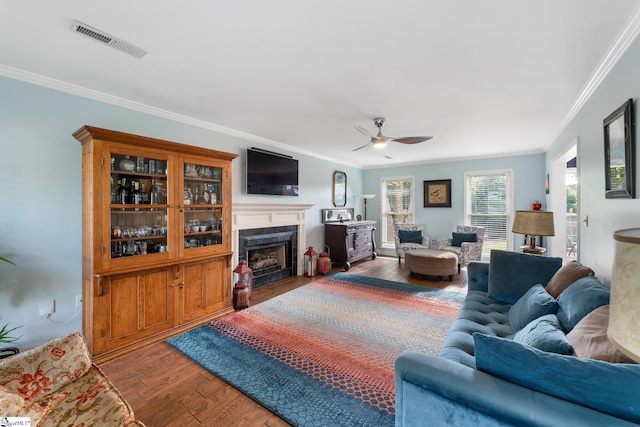 living area with visible vents, ornamental molding, wood finished floors, a fireplace, and a ceiling fan