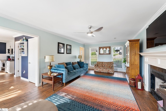 living room with ceiling fan, crown molding, a tile fireplace, baseboards, and hardwood / wood-style floors