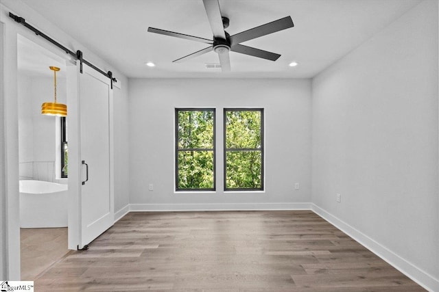 unfurnished bedroom with wood finished floors, recessed lighting, a barn door, and visible vents