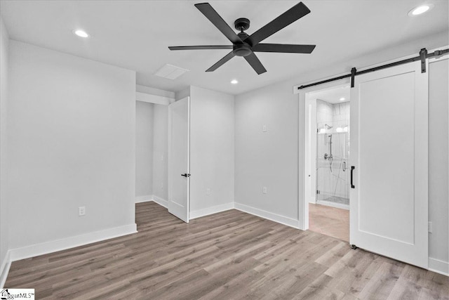 unfurnished bedroom featuring a barn door, ensuite bath, recessed lighting, baseboards, and wood finished floors