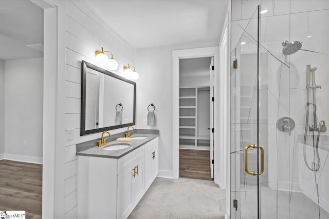 bathroom featuring a sink, baseboards, a shower stall, and double vanity