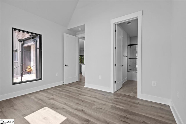 unfurnished bedroom with baseboards, ensuite bathroom, vaulted ceiling, and wood finished floors