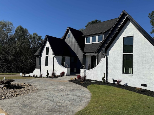 view of front of house featuring crawl space, a front yard, roof with shingles, brick siding, and curved driveway
