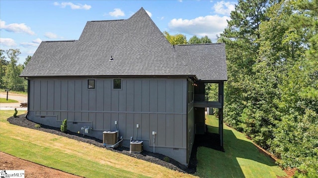 view of property exterior featuring a deck, roof with shingles, central AC unit, board and batten siding, and a yard