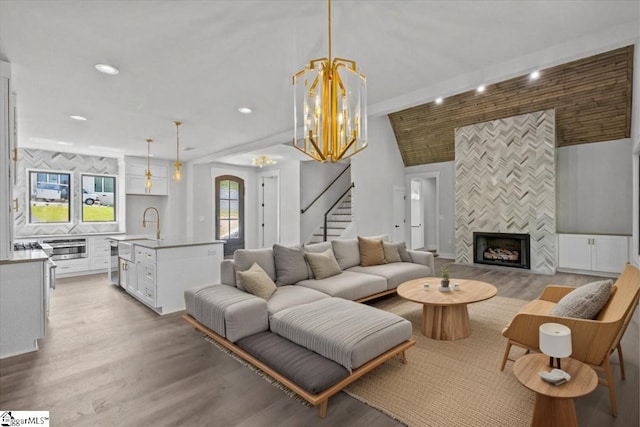 living room with an inviting chandelier, light wood-style flooring, recessed lighting, a tile fireplace, and stairway