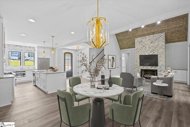 dining room with an inviting chandelier, lofted ceiling, a fireplace, light wood-style floors, and recessed lighting