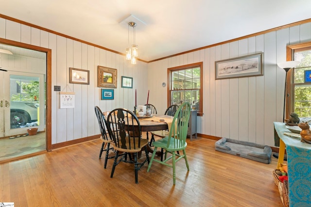 dining room with baseboards, wood walls, ornamental molding, and light wood-style flooring