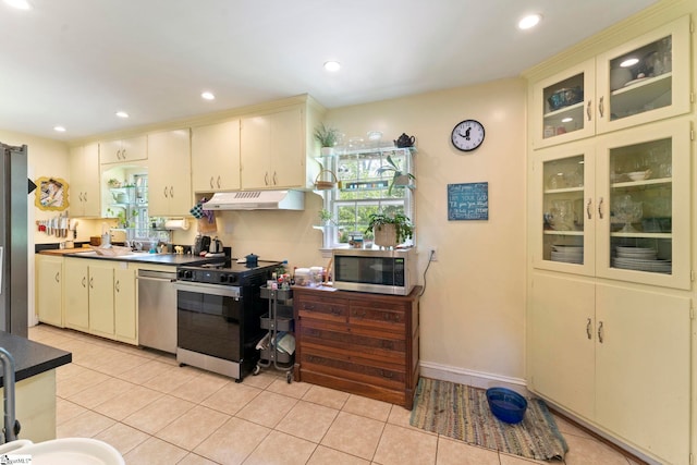 kitchen with cream cabinets, under cabinet range hood, appliances with stainless steel finishes, and light tile patterned floors